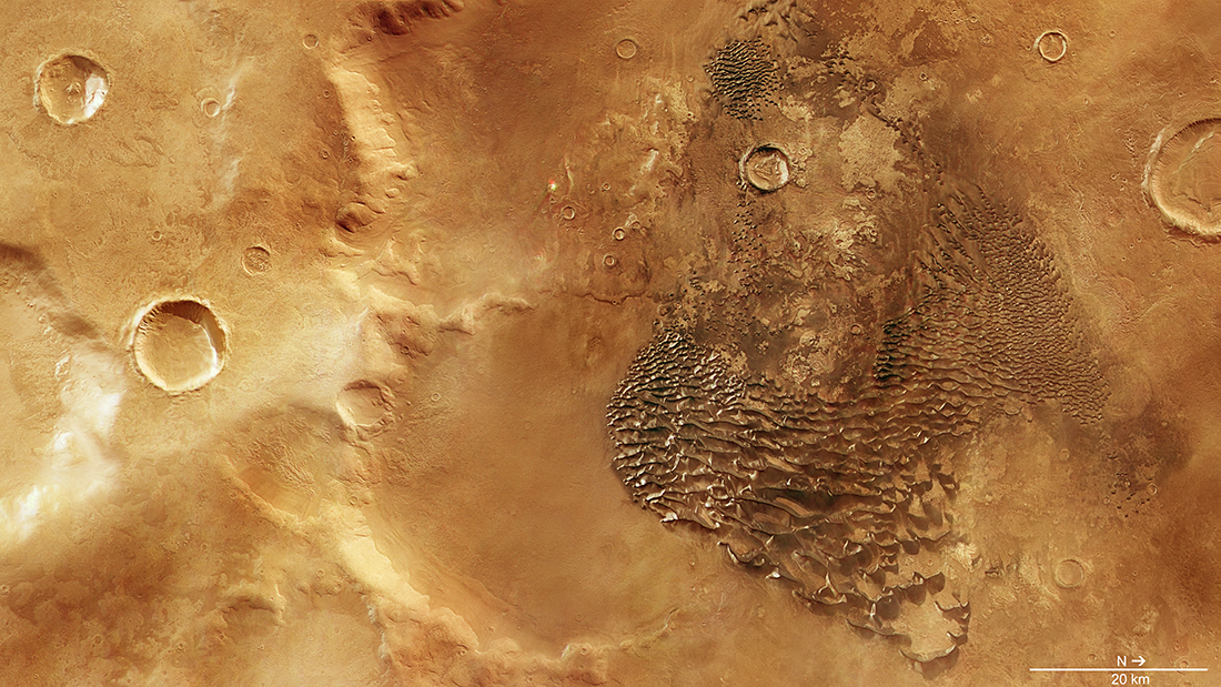 Several craters on the planet mars. On the right, there is a darker patch filled with sand dunes which look like metal waves.